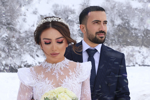 A husband and wife in their wedding attire embrace outside in a snowy landscape.