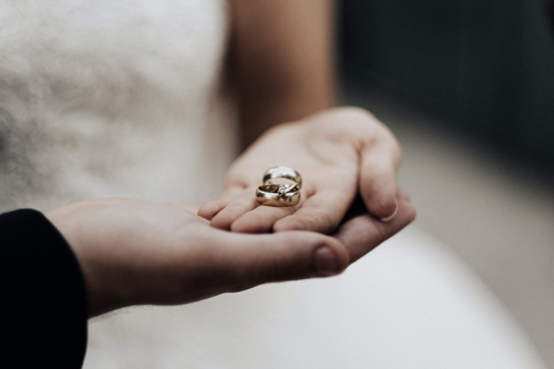 Close-up picture of a person's hands holding engagement rings and wedding bands.
