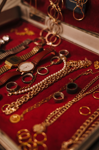 A jewelry box with many compartments open to display gold watches, rings, pearls, and gemstones.