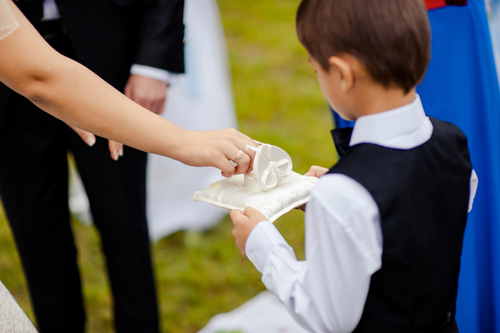 A young ring bearer presenting the rings to a bride and groom on their wedding day.